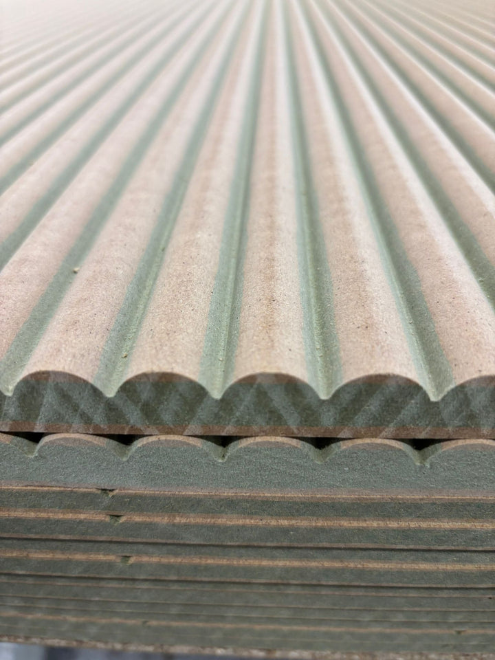 Close-up of stacked ribbed MDF panelling sheets showing rounded ribs and the shaped sheet edges